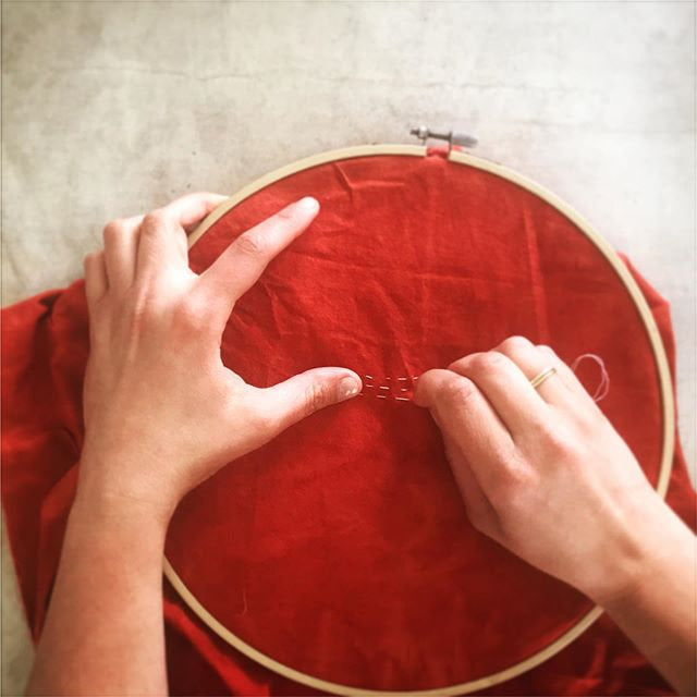 Person stitching on a red fabric inside an embroidery hoop.