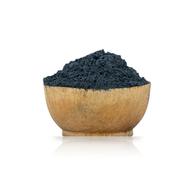 Wooden bowl filled with dark blue powder on a white background