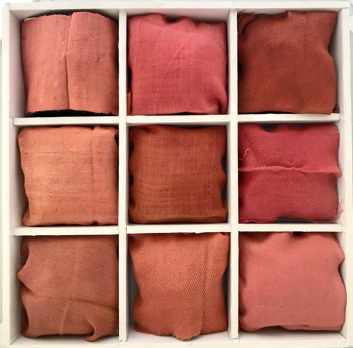 Nine folded fabric swatches dyes qith Alder Buckthorn Bark (Rhamnus frangula) in various red and orange tones arranged in a grid on a white background.