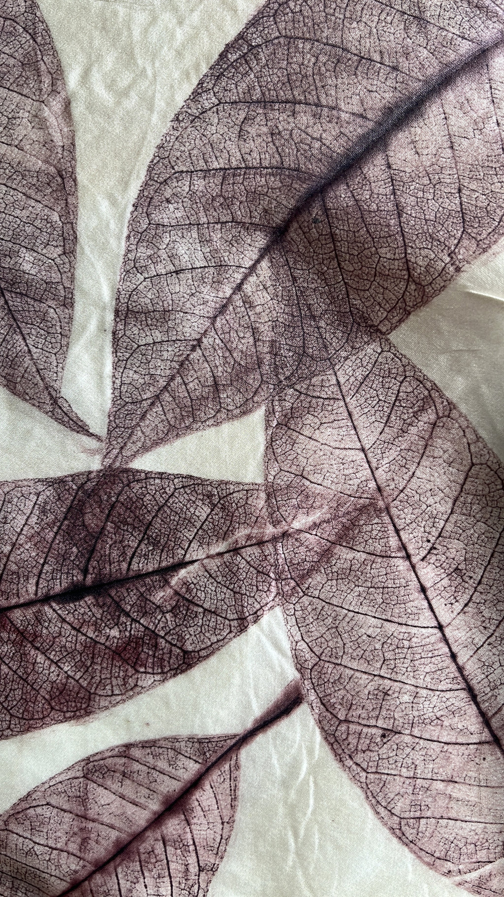 A close-up of a fabric pressed leaf prints with intricate vein details in muted purple and brown tones over a light cream background.