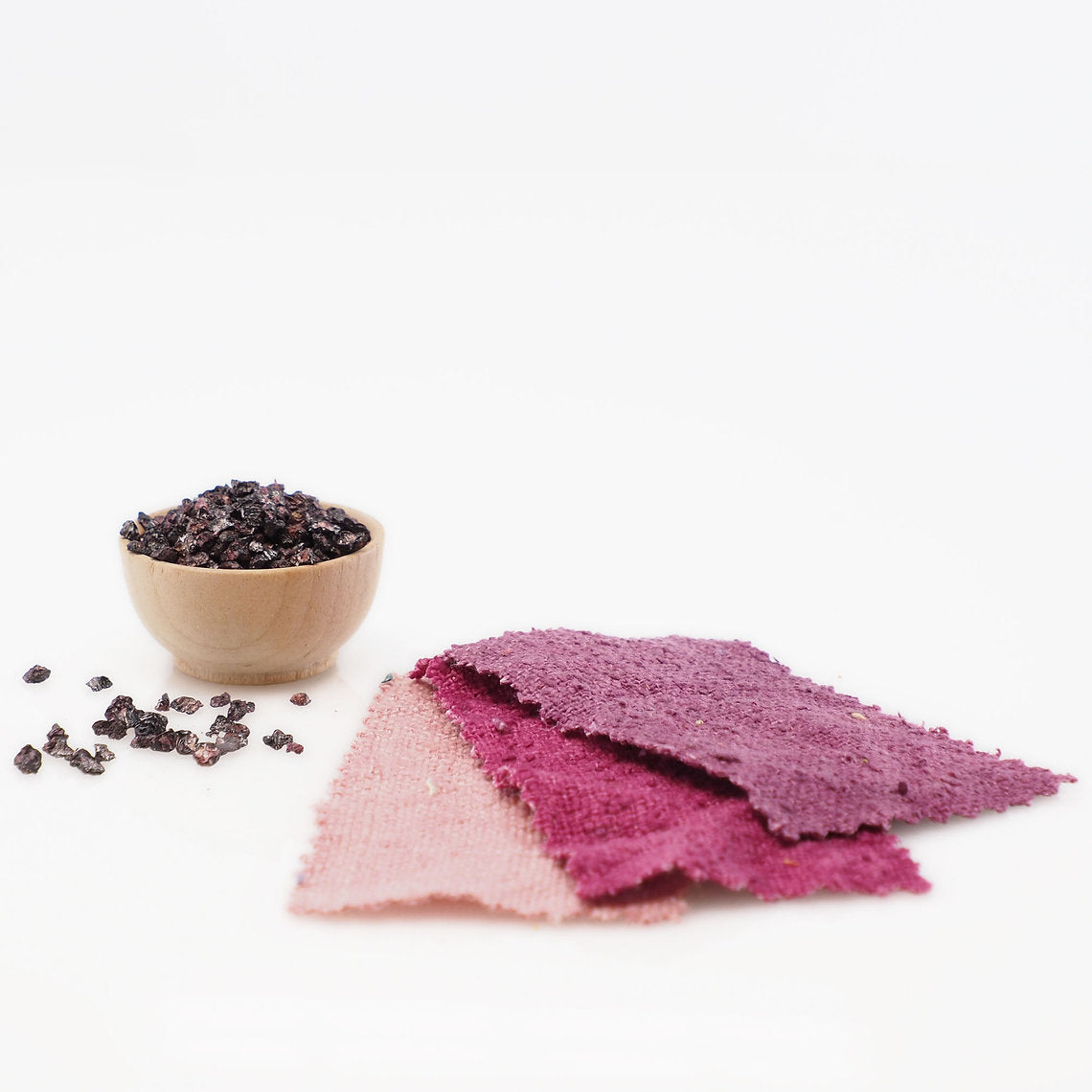Three purple fabric samples on a white background with a small wooden bowl of dark berries.