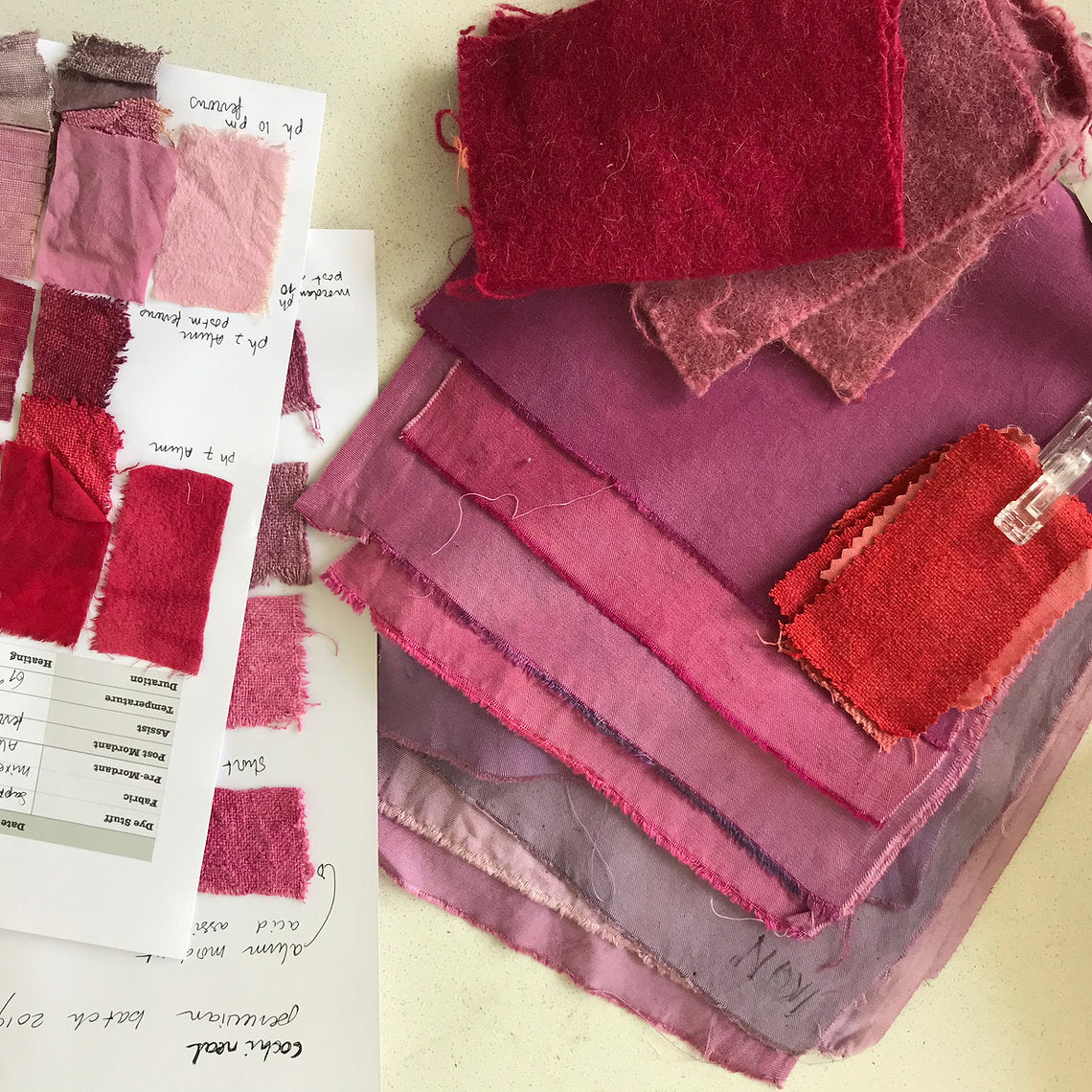 Stack of fabric swatches in red and pink shades with a color chart on a light background