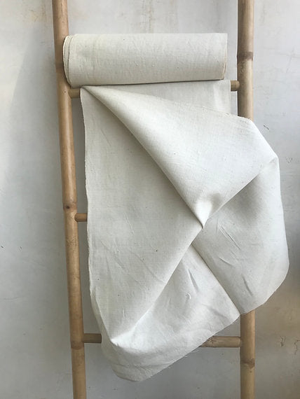 Rolled-up white fabric on a wooden ladder against a plain wall.