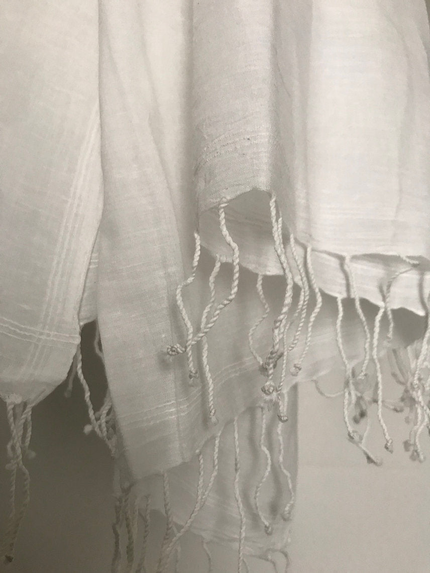 Close-up of a white cotton muslin scarf with frayed edges on a plain background