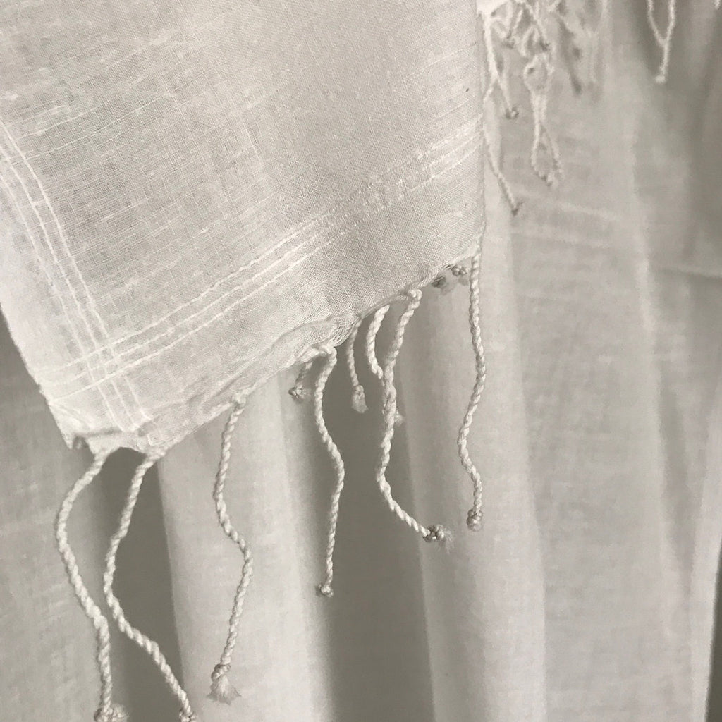 Close-up of a white cotton muslin scarf with fringes on a plain background