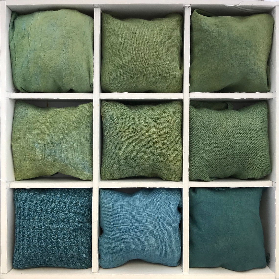 Nine green and blue fabrics dyed Fustic Heartwood Chips (Chlorophora tinctoria) arranged in a grid on a white background.