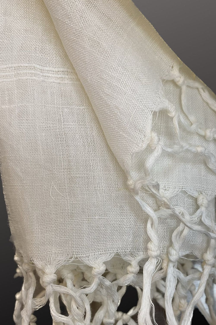 Close-up of a white linen scarf with lace trim on a dark background