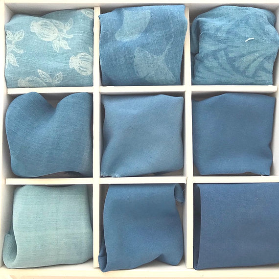 Collection of folded blue fabric pieces arranged in a grid on a light wooden surface.