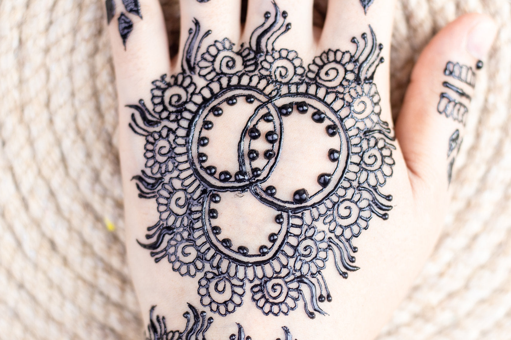 Hand with intricate black henna design on a blurred beige background