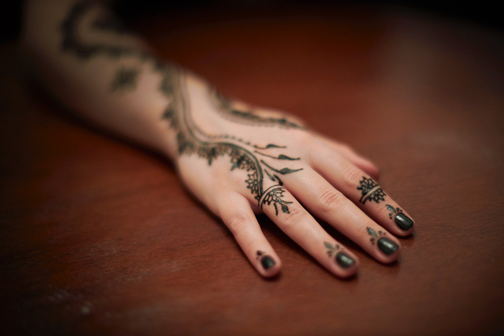 Hand with intricate black henna designs on a wooden surface