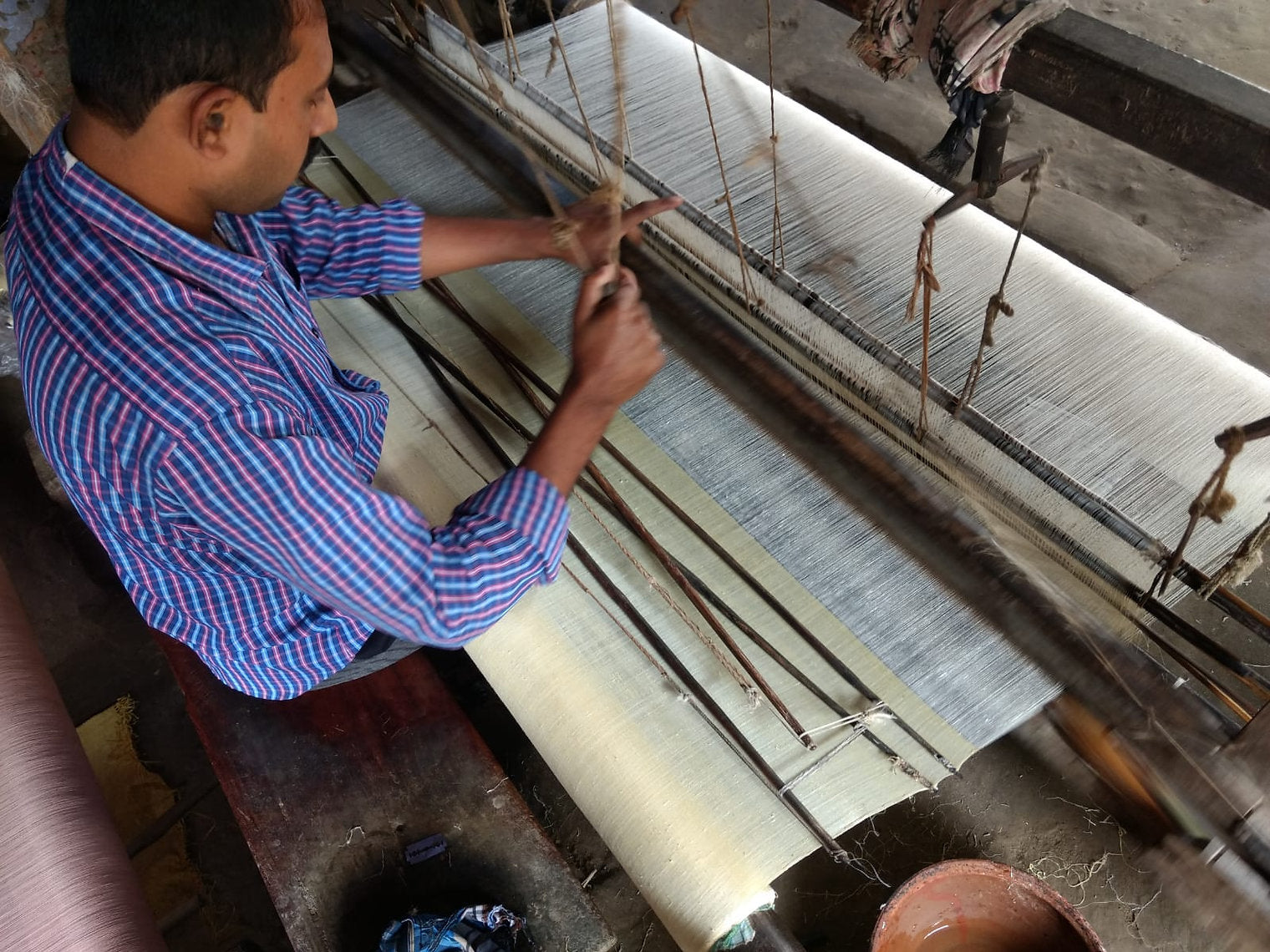Person operating a traditional weaving loom with fabric and threads.