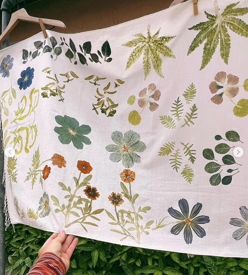 Fabric with floral and leaf pattern held by a hand against a green leafy background