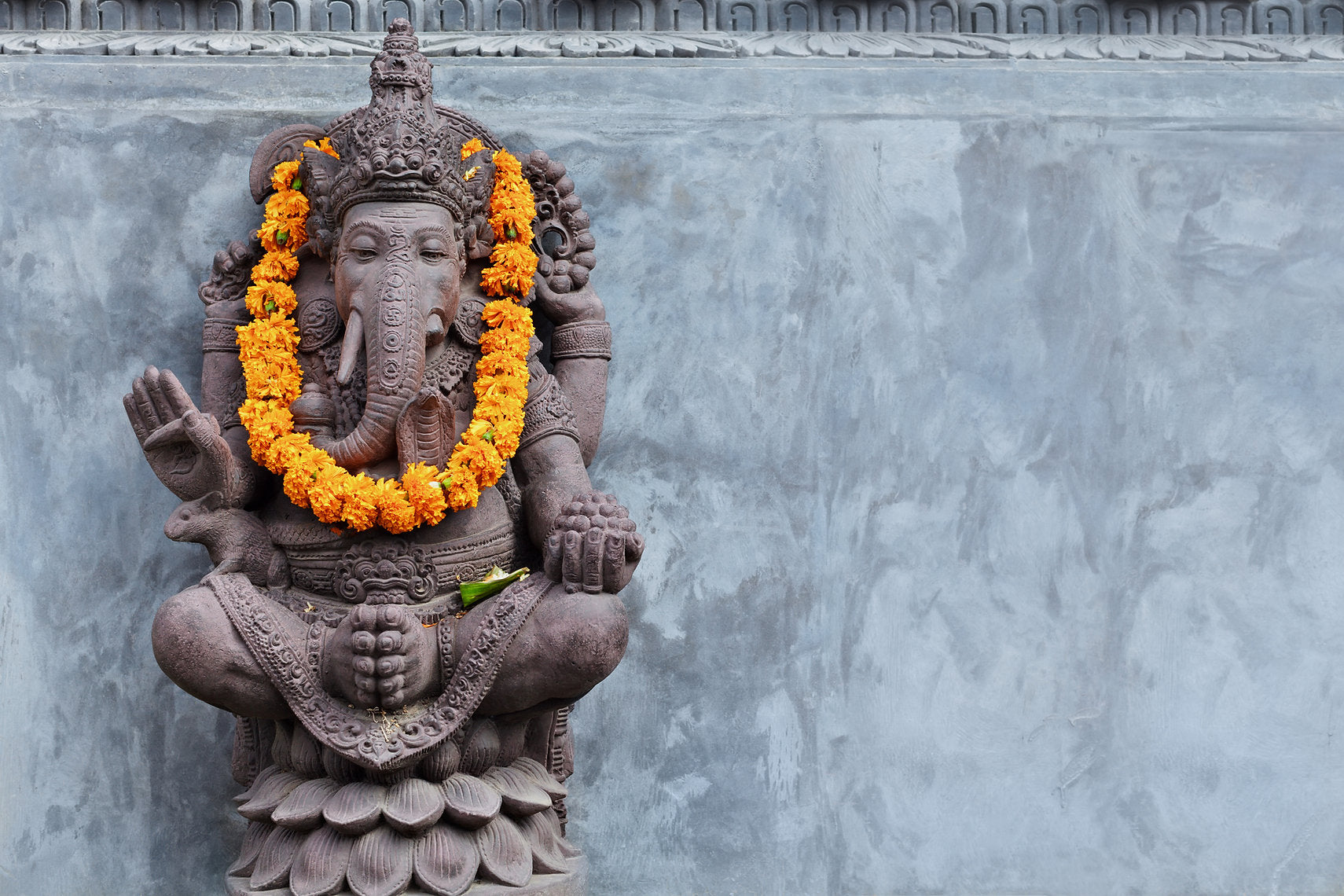 Stone statue of a deity with floral garlands against a gray wall