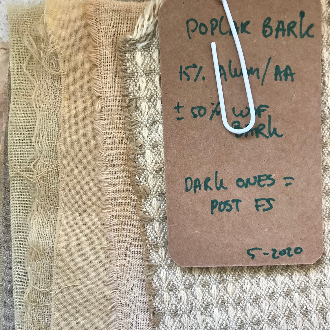 Textured fabric swatches dyed Poplar Bark (Populus nigra) with a label on a textured surface