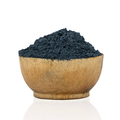 Wooden bowl filled with dark blue powder on a white background