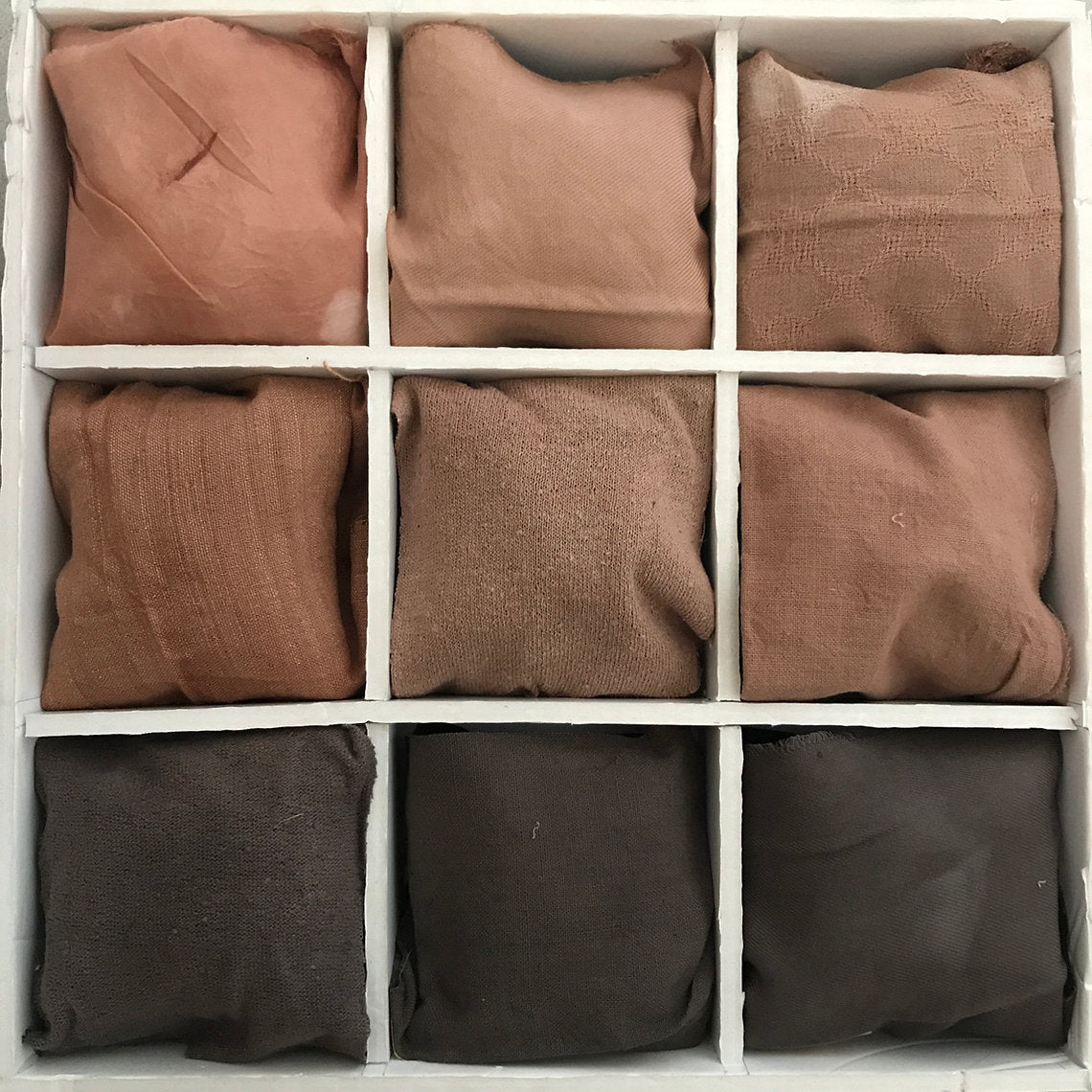 Nine folded brown fabrics dyed Quebracho Rojo Extract (Schinopsis lorentzii) II arranged in a 3x3 grid on a white background.