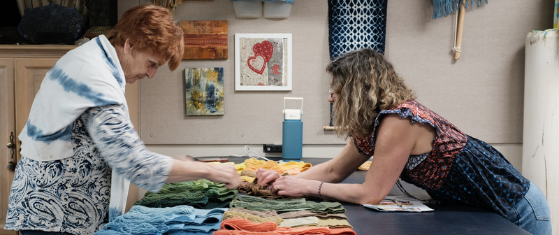 Two women in a kitchen preparing food with vegetables on a table.