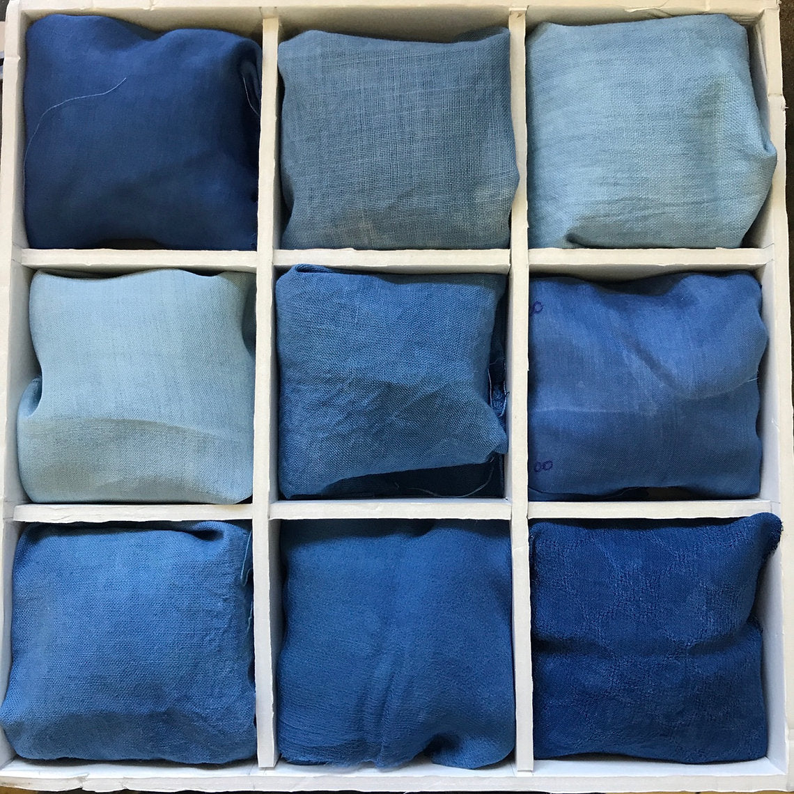 Nine blue fabric samples dyed Woad Powder (Isatis Tinctoria) arranged in a grid on a white background