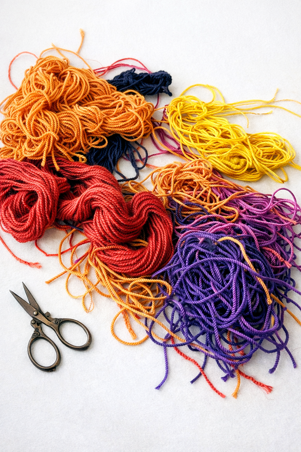 Colorful yarn skeins in orange, red, yellow, and purple with a pair of scissors on a white background.